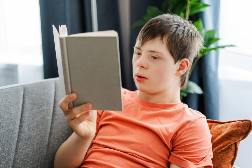 eenager with down syndrome reading a book on a sofa